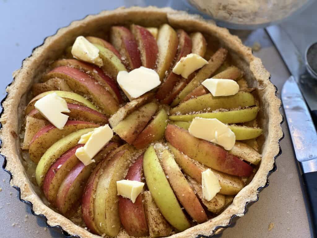 Sliced apples in an apple tart with chunks of butter on the top