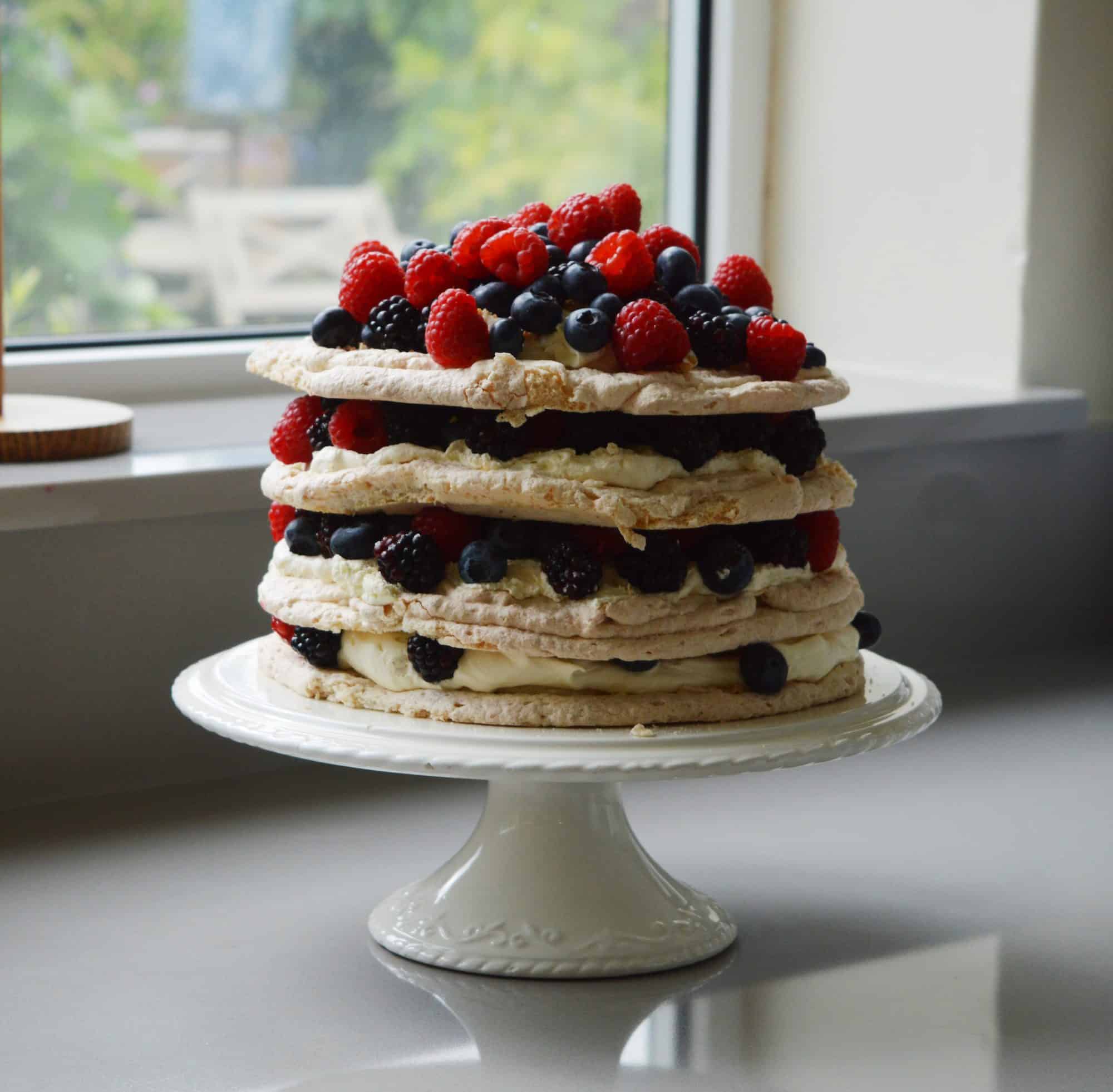 Layers of meringue fruit and cream on a white cake stand