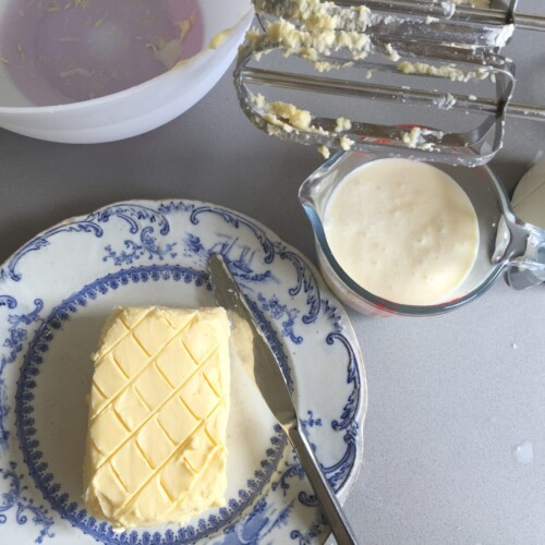 Freshly made and shaped butter on a blue plate with the buttermilk in a jug by the side.