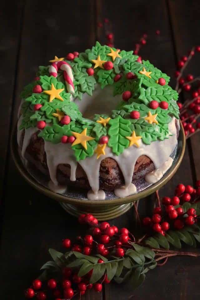 bundt style cake topped with white icing and fondant holly leaves, berries and stars