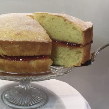 victoria sandwich on a glass cake stand with a serving knife