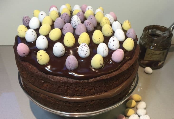 Chocolate Cake Decorated with sugar coated eggs. On a glass cake stand.