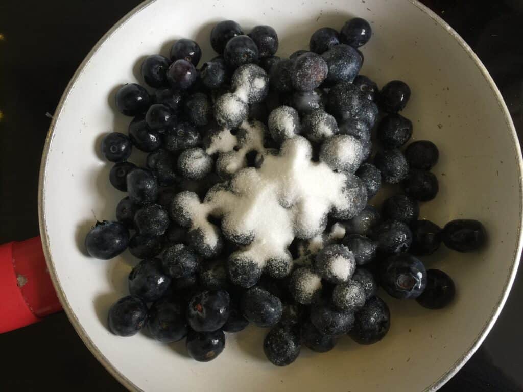 Blueberries sugar and water in a small shallow pan.