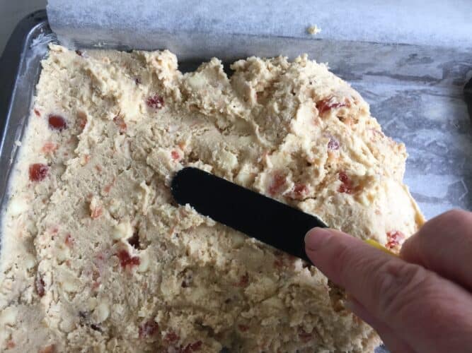 Spreading cookie dough into a shallow baking tin with a small spatular.