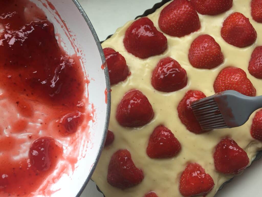 close up shot of strawberries being glazed for the vanilla sheet cake.