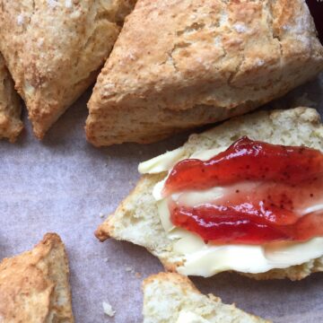 A round of baked scones. One sliced with butter and jam.