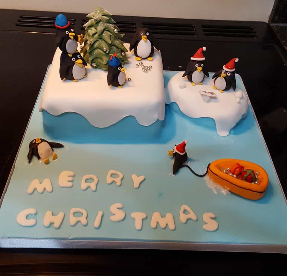 Cake with Fondant cake toppers shaped like penguins wearing santa hats and a christmas tree