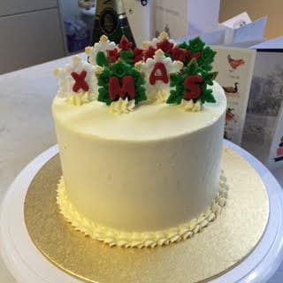 White cake with buttercream edging and upright red white and green fondant leaves spelling merry xmas
