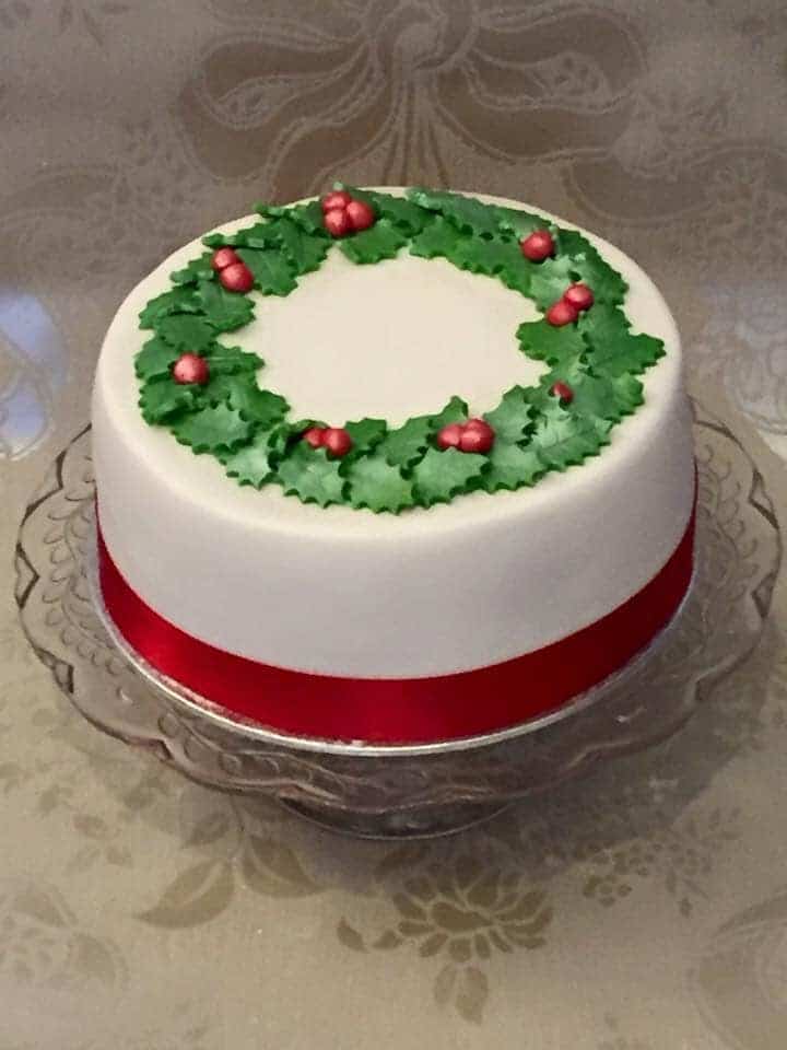 Decorated Christmas cake with white fondant, red ribbon around the base, and fondant holly wreath