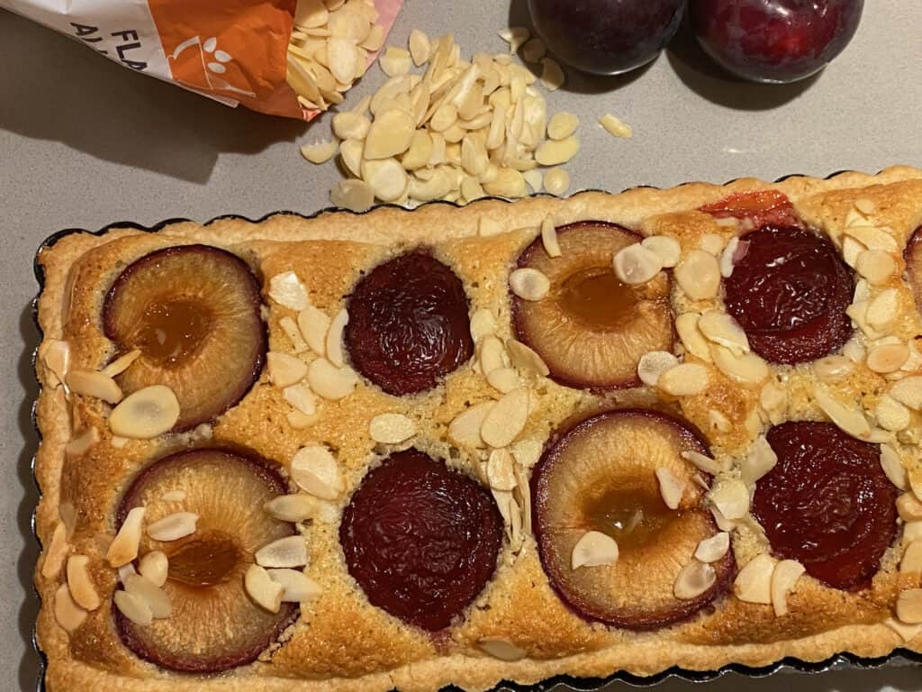 Baked Tart on a counter top with Flaked Almonds and Plums