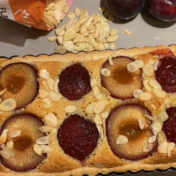 Baked Tart in a rectangular tin with Flaked Almonds and Plums on the counter top.