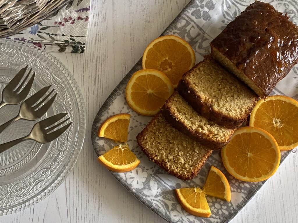 Orange Loaf Cake sliced on a grey plate with dishes and forks