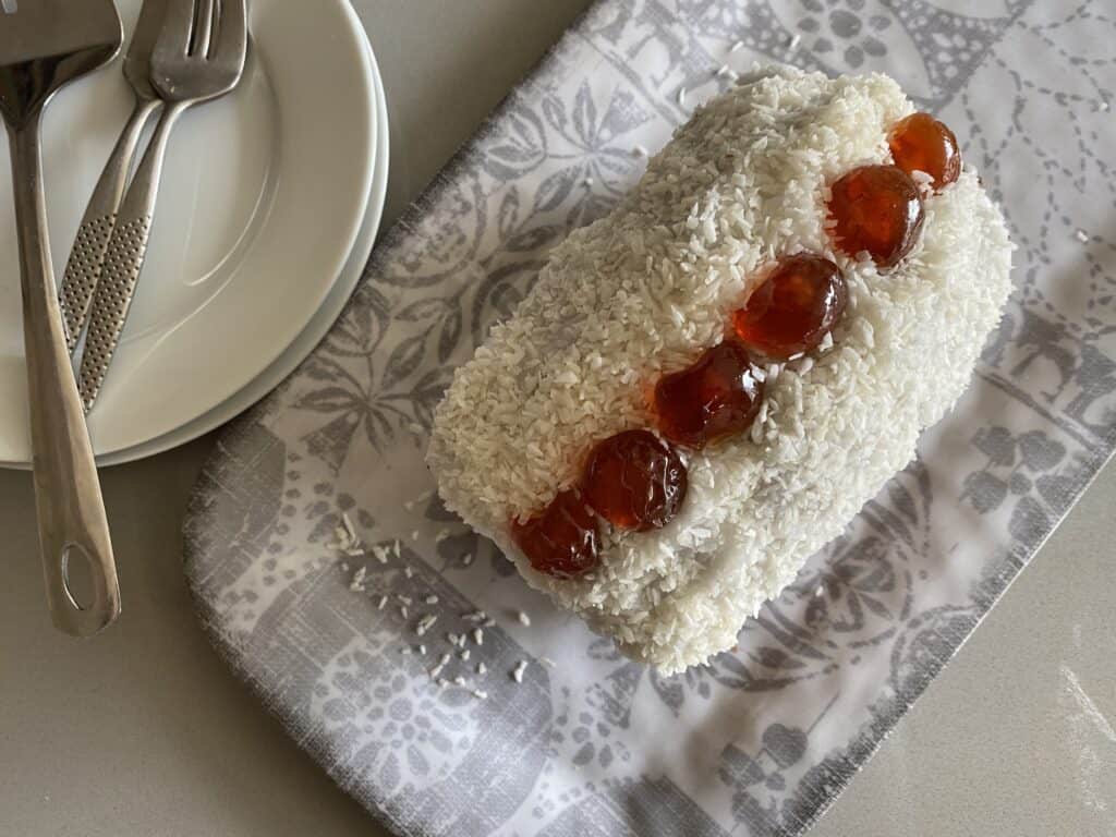 Cherry and Coconut cake on a grey dish. With a small white plate and dessert forks.