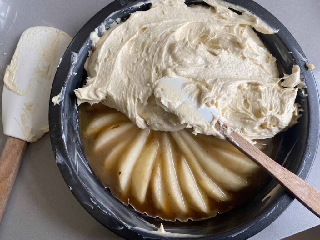 Cake batter spread over sliced pears in a tin.