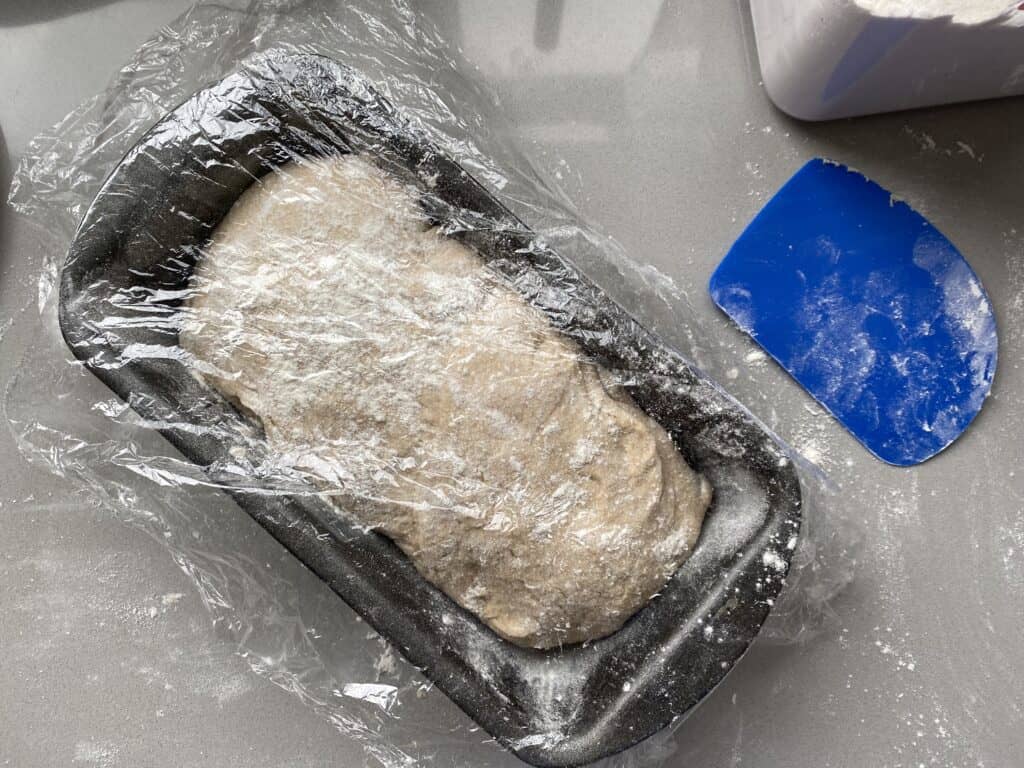 Cling film covering bread dough in a tin