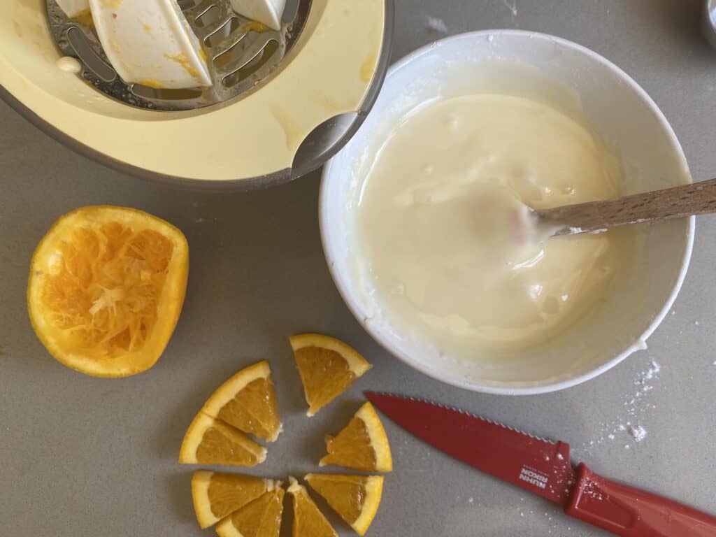 Orange icing in a white bowl with orange slices and red knife