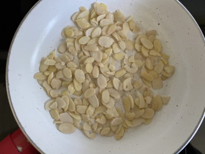 Untoasted Flaked Almonds in a small frying pan.