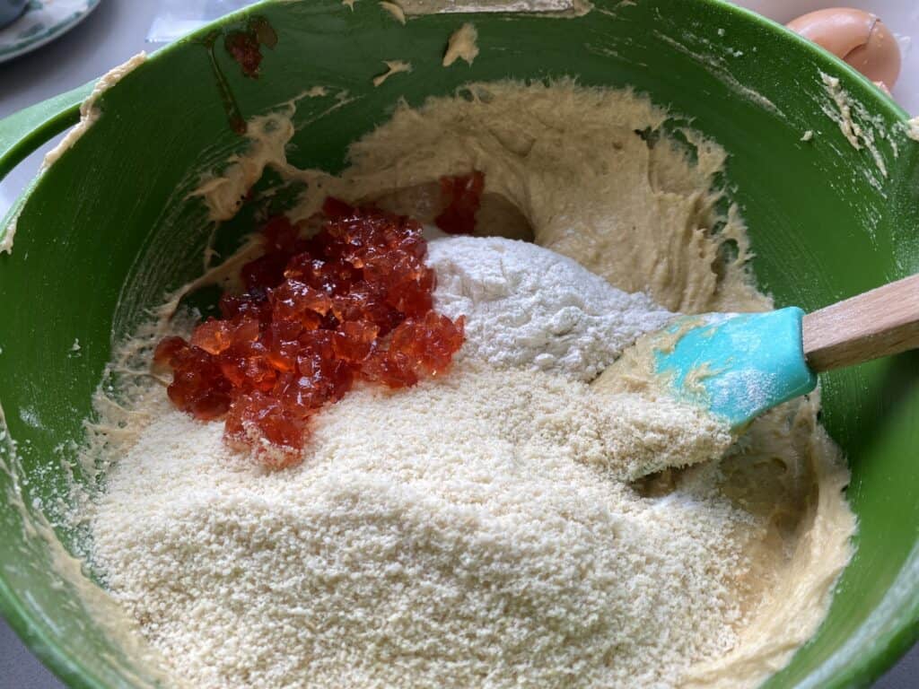 Chopped Red cherries, flour and cake batter in a green mixing bowl