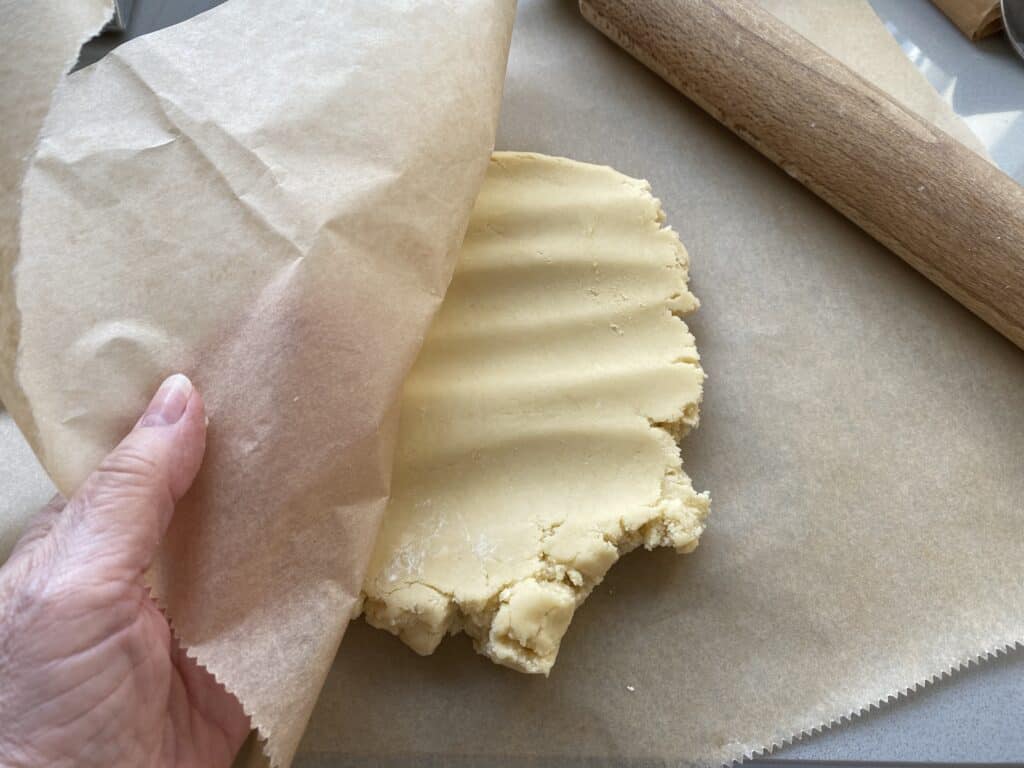 Biscuit dough between baking parchment with a rolling pin on the side