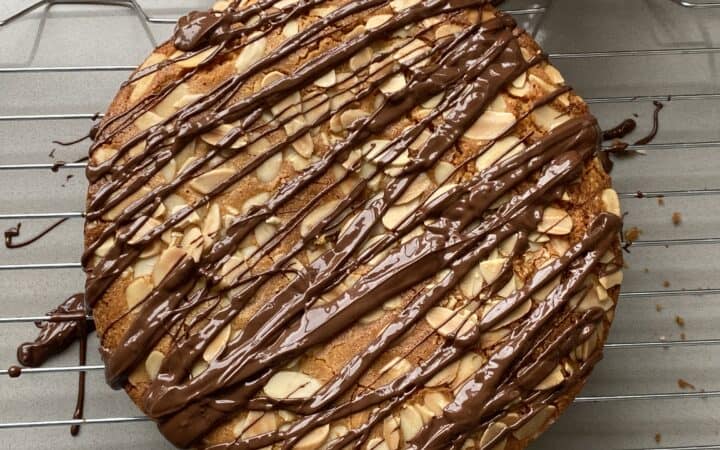 Ground Almond Cake with flaked almonds and chocolate Drizzle. on a cake rack