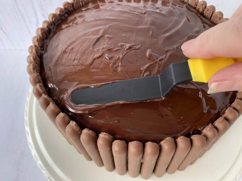 Spreading chocolate over the top of a cake using a small spatular